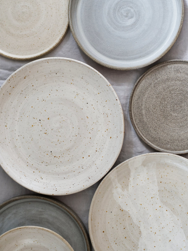 Unieke handgemaakte keramieken borden in zachte aardetinten, naast elkaar van bovenaf gefotografeerd op een tafel.