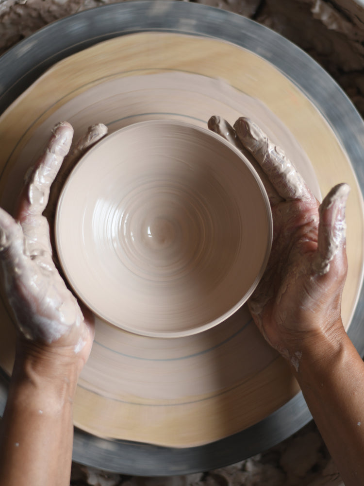 Handen met klei van iemand achter de pottenbakkersschijf