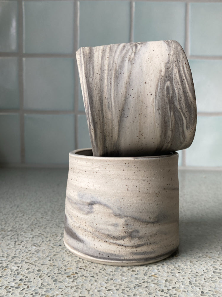 Twee handgemaakte kopjes gedraaid van drie kleuren klei, opeen gestapeld, aardse kleuren