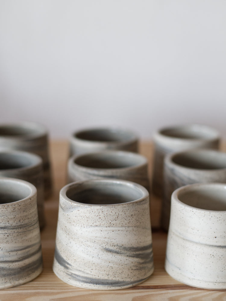 Drie handgemaakte kopjes, gedraaid van drie kleuren klei in rijen naast en achter elkaar opgesteld