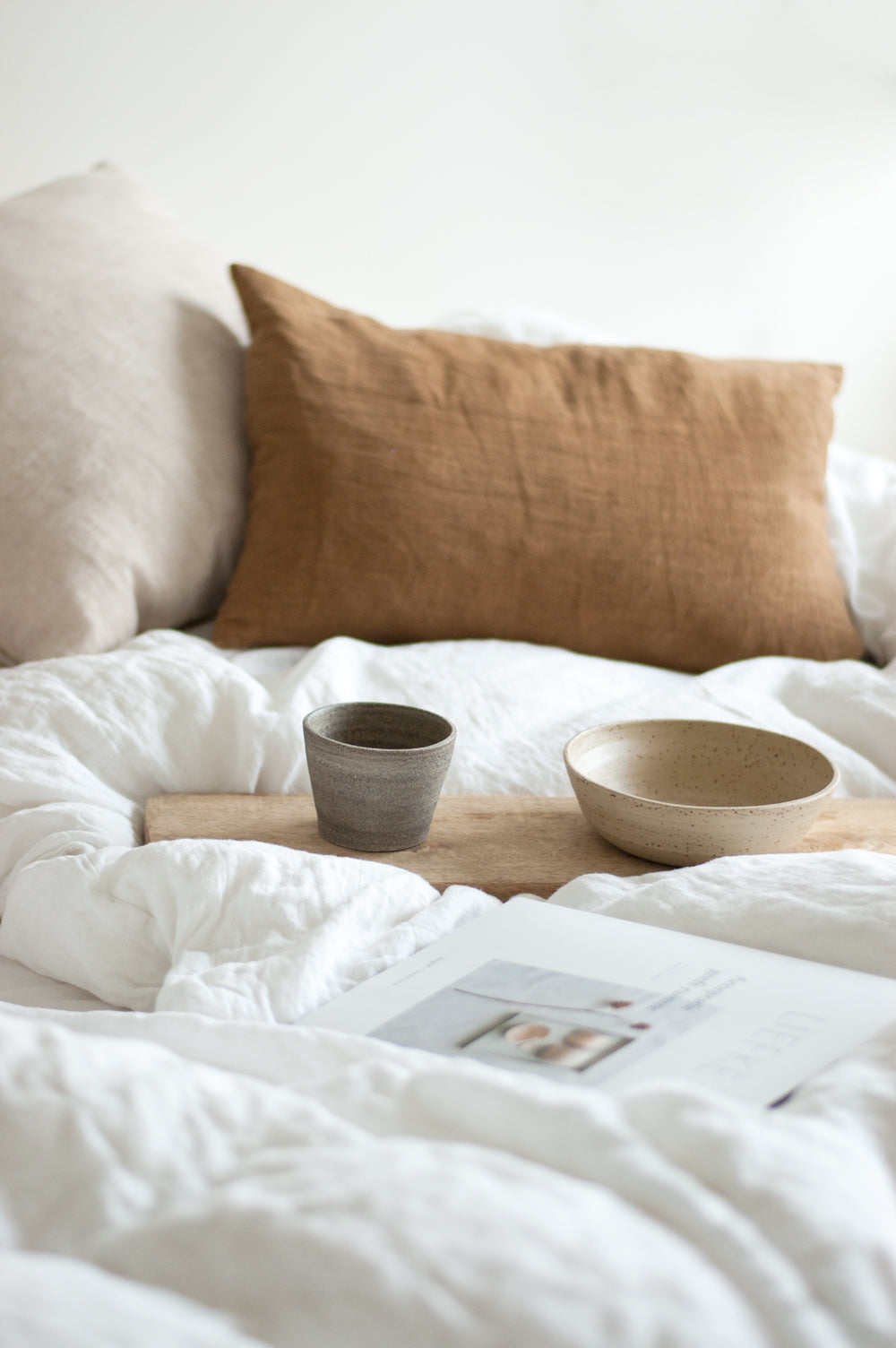 Opgemaakt bed met linnen beddengoed en daarop een plankje met zelfgemaakt kopje en schaaltje
