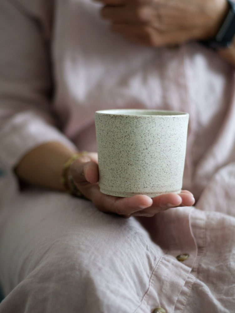 Handgemaakt licht gespikkeld kopje vastgehouden door een hand.