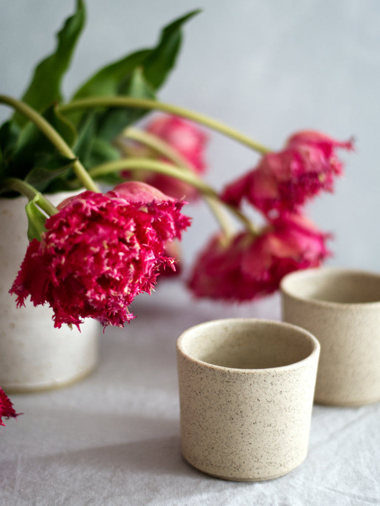 Handgemaakte lichte gespikkelde keramieken kopjes met een vaas met bloemen