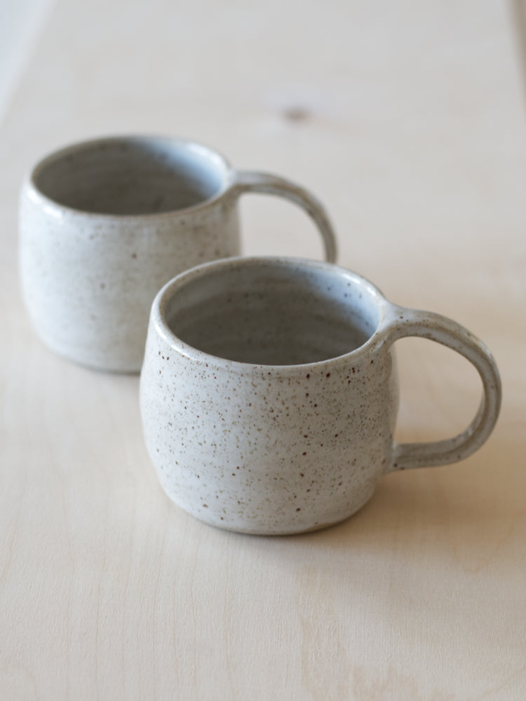 Handgemaakte mokken wit gespikkeld glazuur op lichthouten ondergrond gefotografeerd
