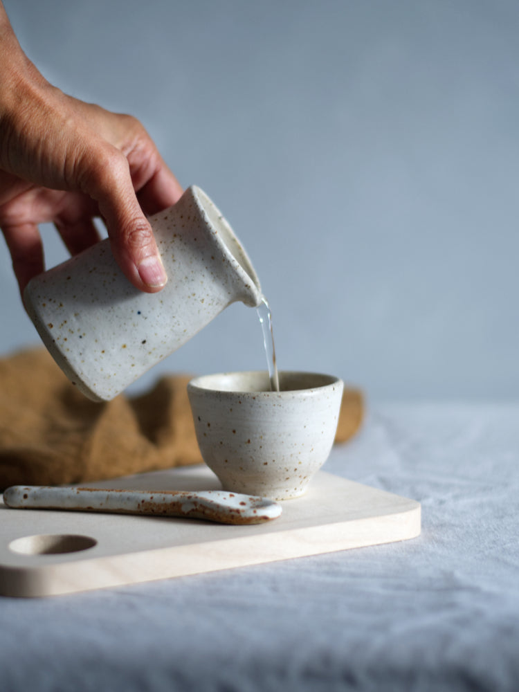 Hand die een schenkkannetje vasthoudt en schenkt in een kopje