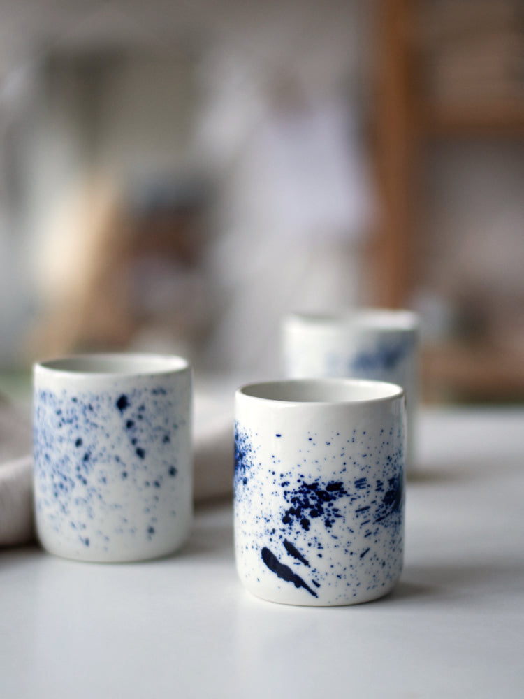 Handgemaakte blauwe gespikkelde kopjes van porselein naast een theedoek op een witte tafel