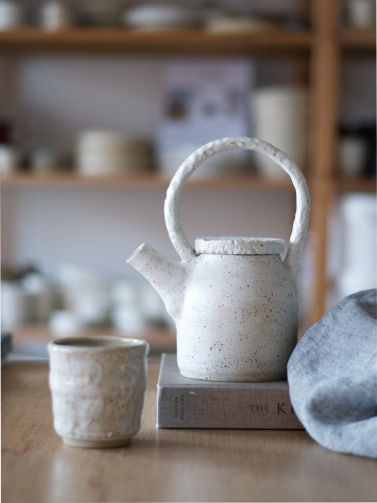 Handgemaakte theepot met uitgesneden reliëf handvat en deksel op boek met theedoek en kopje