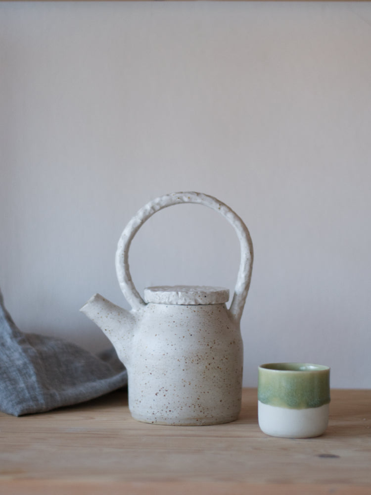 Handgemaakte theepot met whitewashed en relief deksel en handvat met een kopje ernaast gefotografeerd