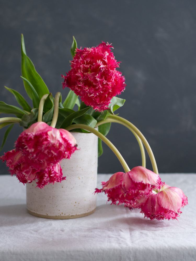 Roze bloemen in een handgemaakte cilinderpot op een tafelkleed