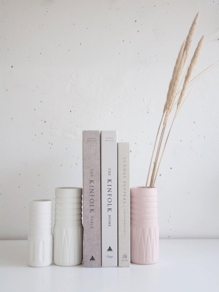 Gekleurde porseleinen vaasjes, waartussen een paar boeken staan op een witte tafel. Fotocredits: Sisilia Tiseli
