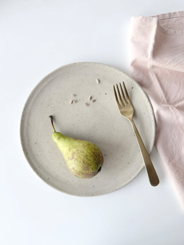 Handgemaakt dinerbord van keramiek met vork, peer met zonnebloemzaadjes en theedoek ernaast