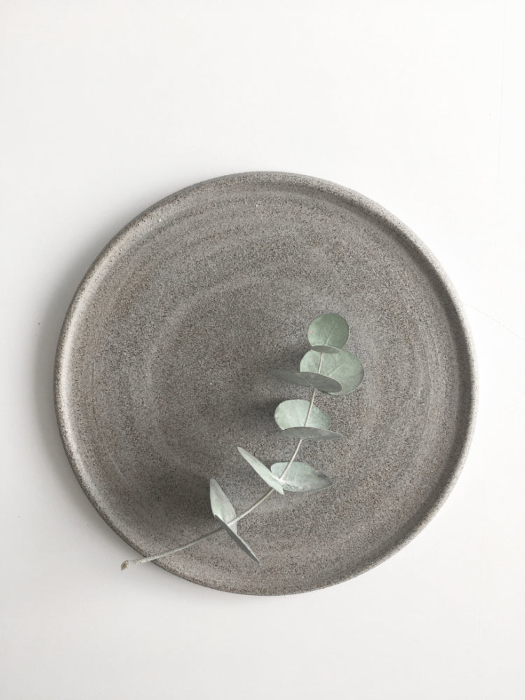 Donker handgemaakt cakebord van keramiek met een eucalyptus takje erop