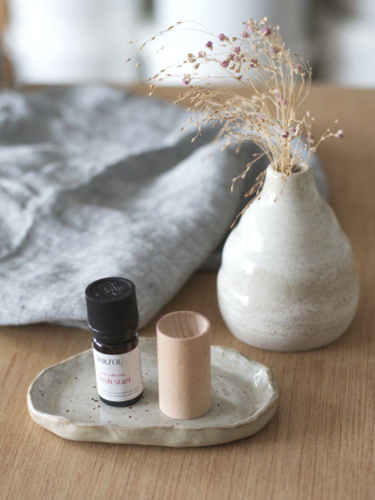 Handgemaakt schaaltje met geurolie en een houten diffuser op een houten ondergrond en zelfgemaakt vaasje ernaast.