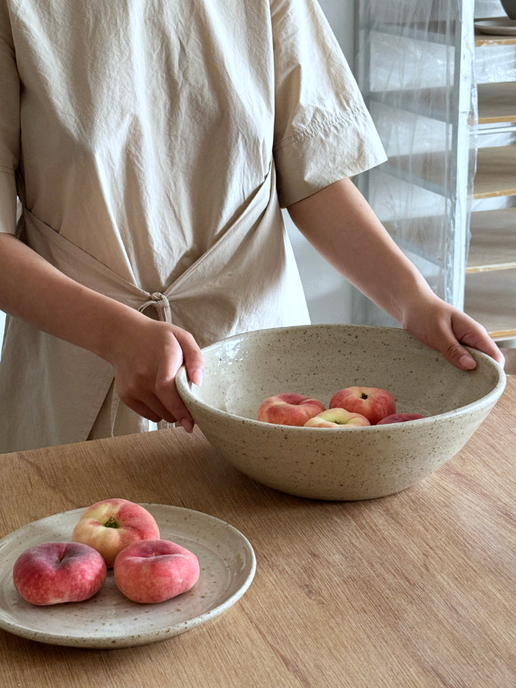 grote handgemaakte keramieken schaal met perziken vastgehouden in handen