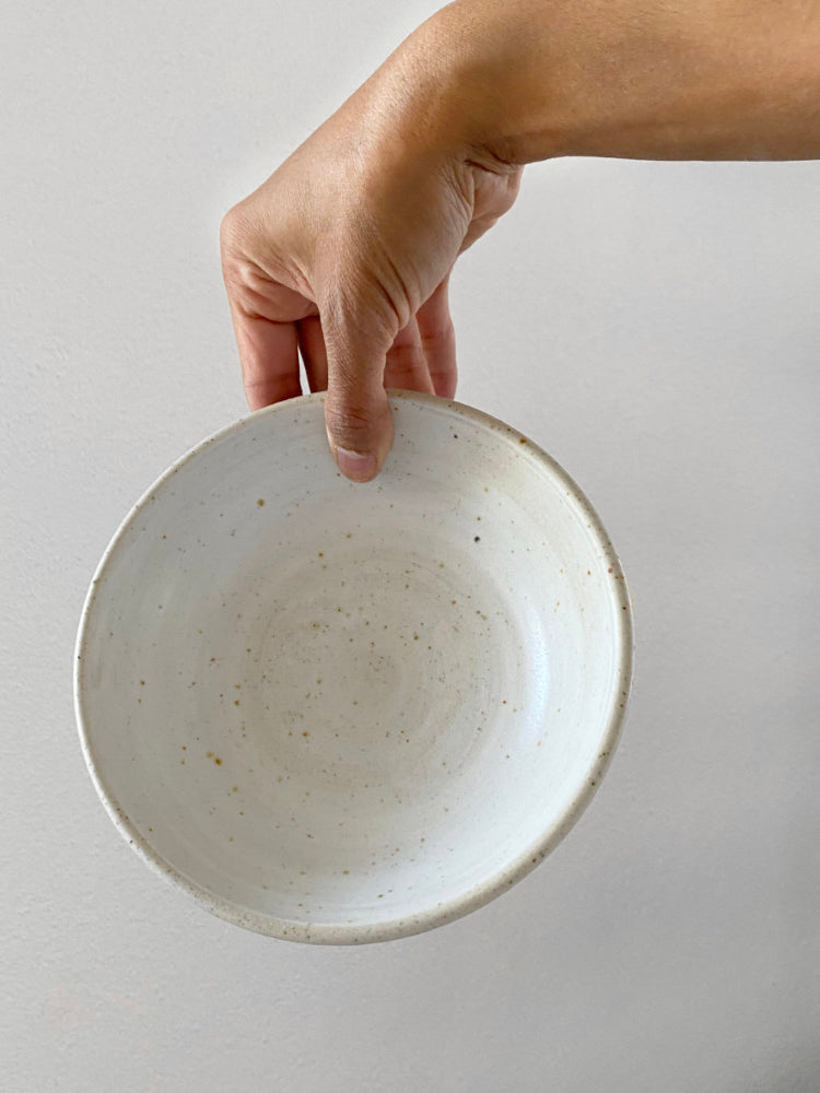 Hand houdt handgemaakte whitewashed keramieken kom vast voor een witte achtergrond