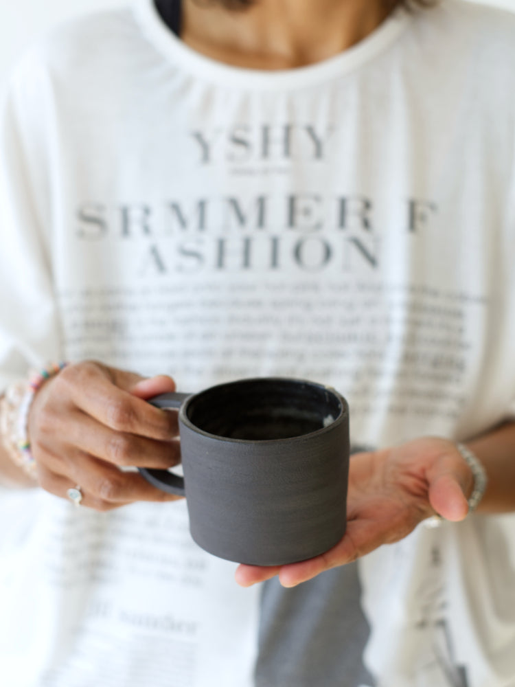 Twee handen die een zwarte handgemaakte mok vasthouden met vervaagde achtergrond