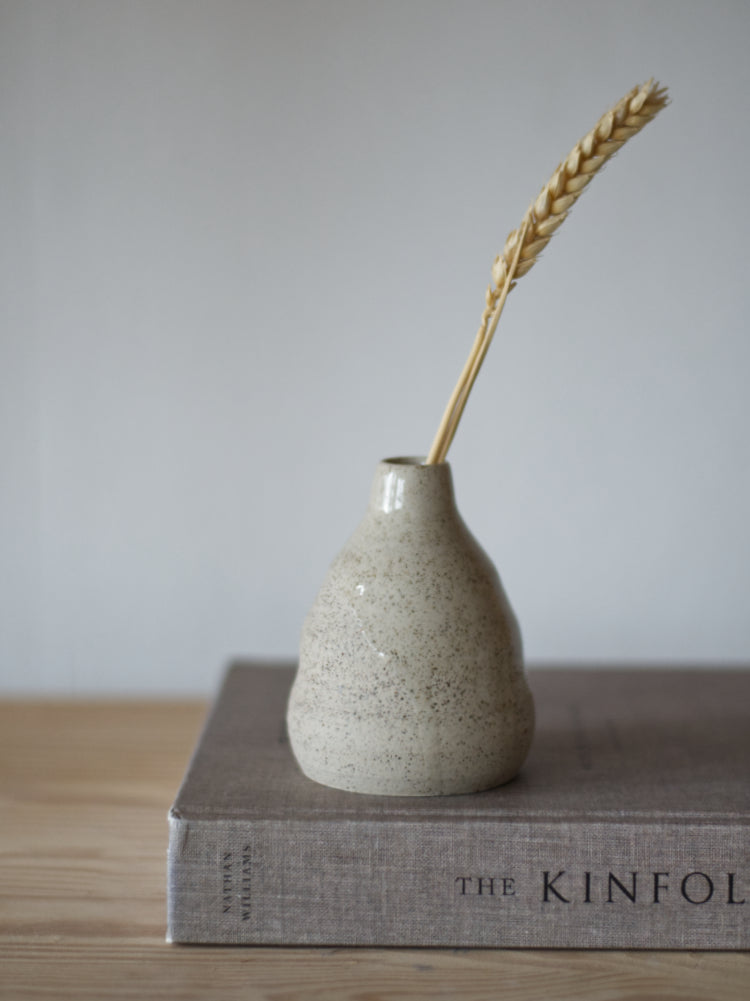 Handgemaakt klein vaasje, gemaakt van gespikkelde klei met licht golvende vorm met een grashalm op een boek
