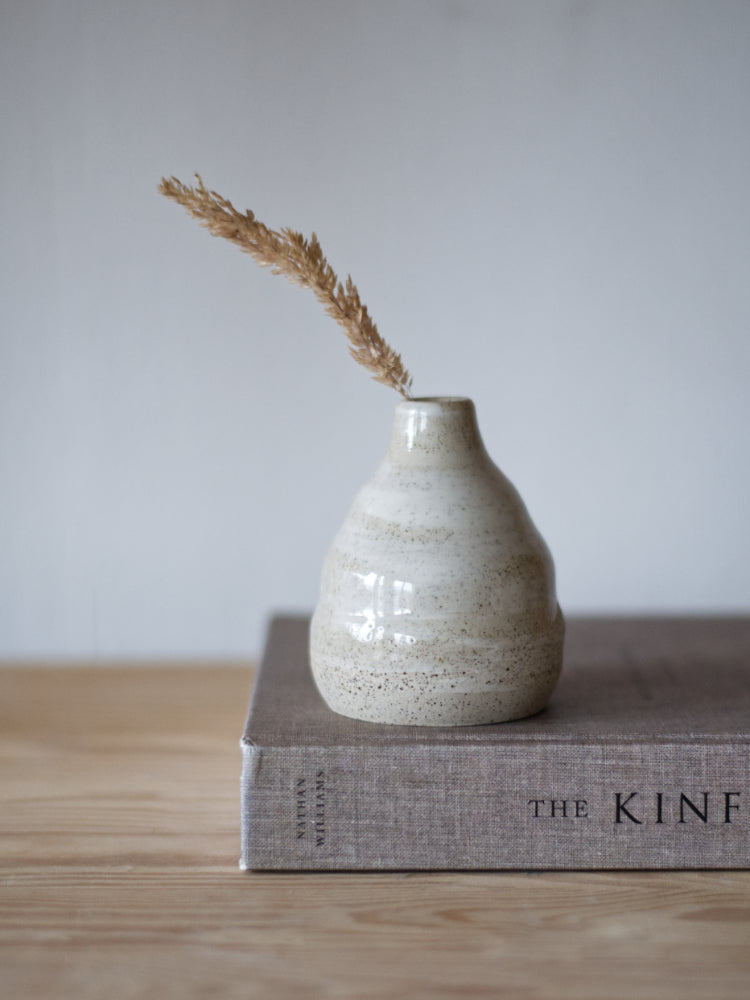 Handgemaakt klein vaasje, gemaakt van gespikkelde klei met licht golvende vorm met een grashalm op een boek gefotografeerd