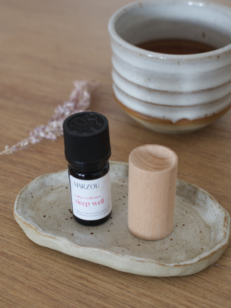 Handgemaakt keramisch schoteltje met geurolie, houten diffuser en theekopje op tafel