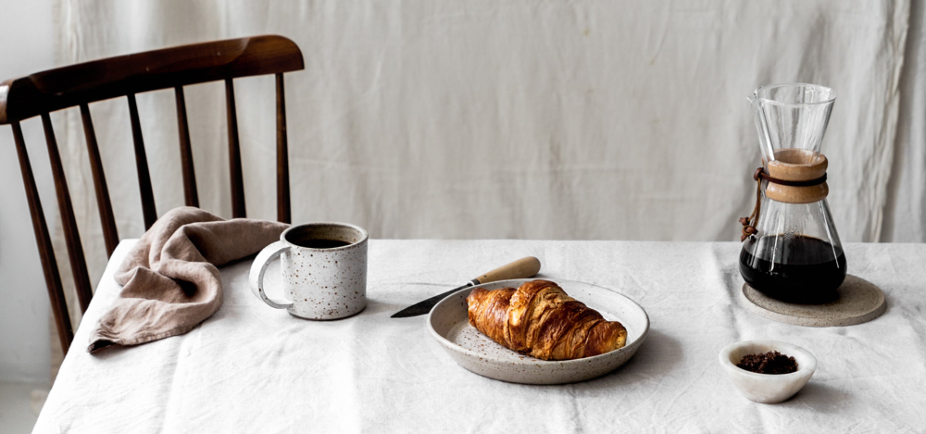 Handgemaakt keramieken servies op een gedekte tafel met stoel en tafelkleed. Ambachtelijk design voor een sfeervolle maaltijd