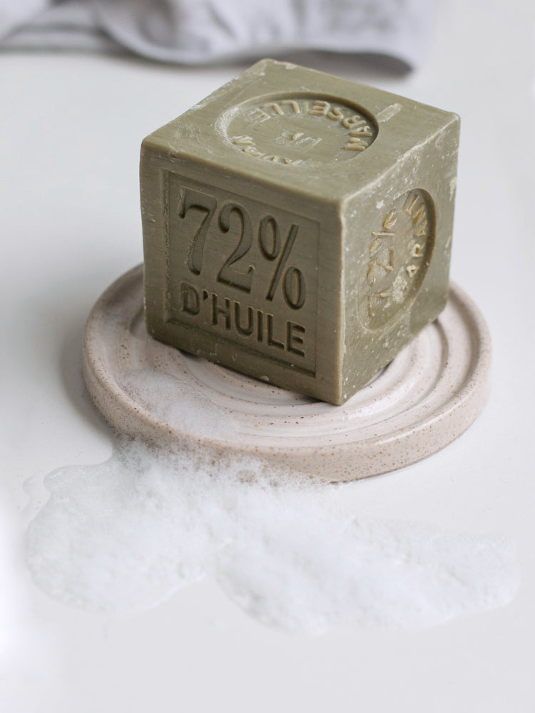 Handgemaakt zeepbakje van keramiek met een groen blok Marseille zeep erop en schuim