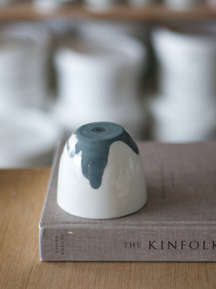 Handgemaakte Waterlijn kopje Large van wit porselein met een donkergrijze waterlijn, onderzijde gefotografeerd. Staand op een boek met linnen kaft, op een houten tafel