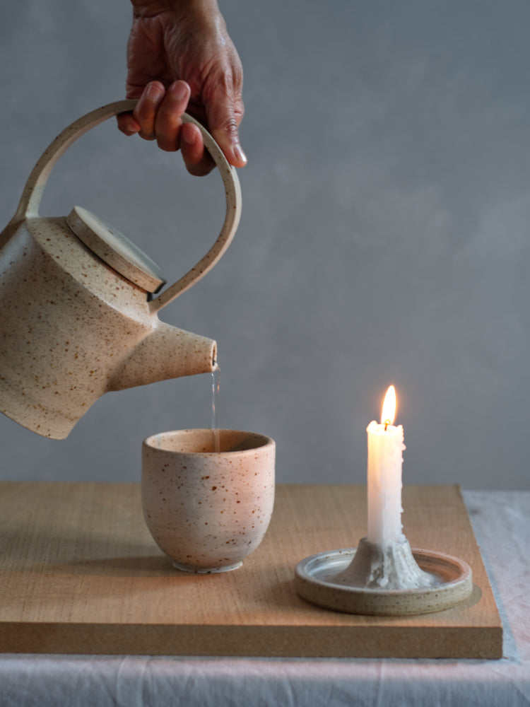 Handgemaakte keramiek kandelaar met theepot die schenkt in een kopje
