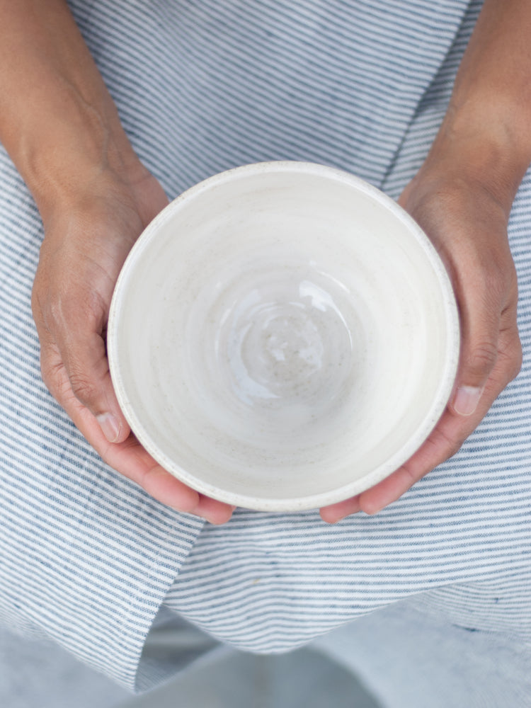 twee handen in een schoot met gestreept schort houden handgemaakte keramieken kom vast