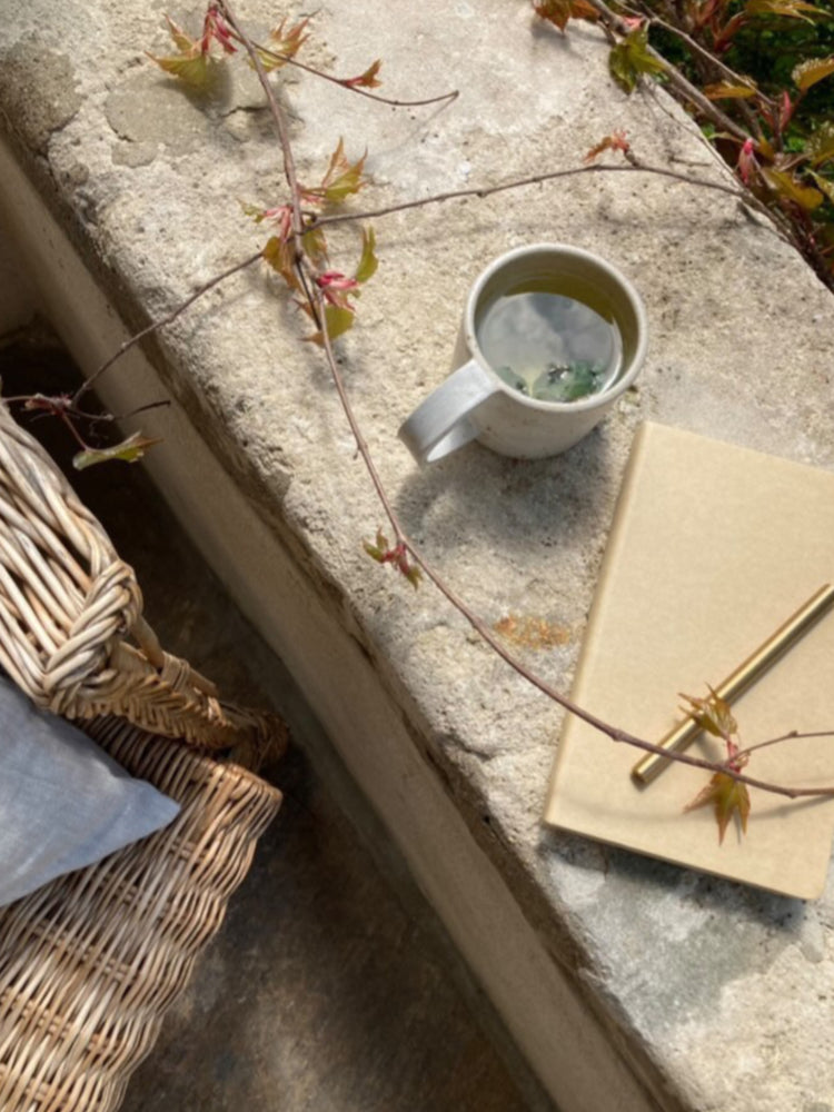 Handgemaakte keramieken mok op een stenen muurtje met een notitieboek en klimop, sfeervol buiten in slow living stijl