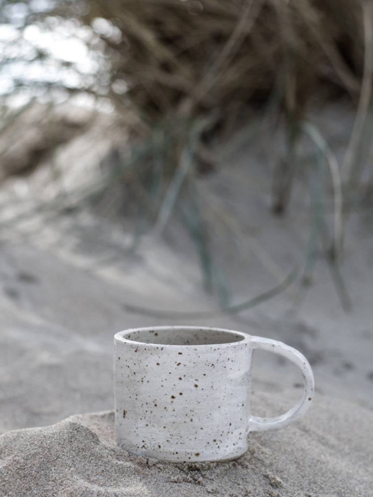 Handgemaakte keramieken mok in de duinen, staand in het zand met duingras eromheen in een natuurlijke strandomgeving