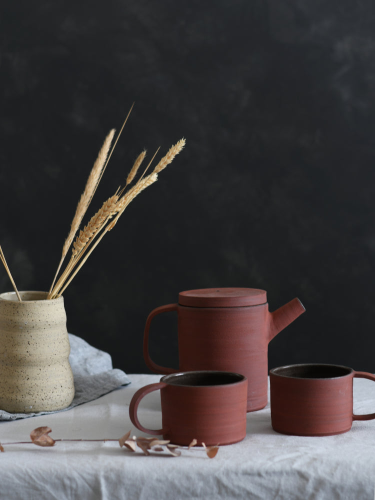 Handgemaakte rode keramieken mokken met een rode theepot op een tafelkleed