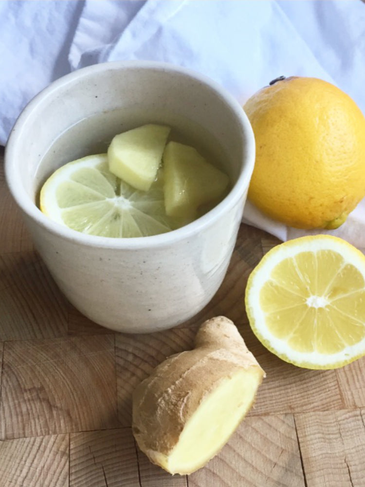 Handgemaakte theekop op een houten snijplank met citroenen en gember