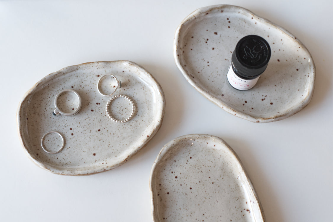 Handgemaakte keramiek schaaltjes met ringen erop en een flesje etherische olie.