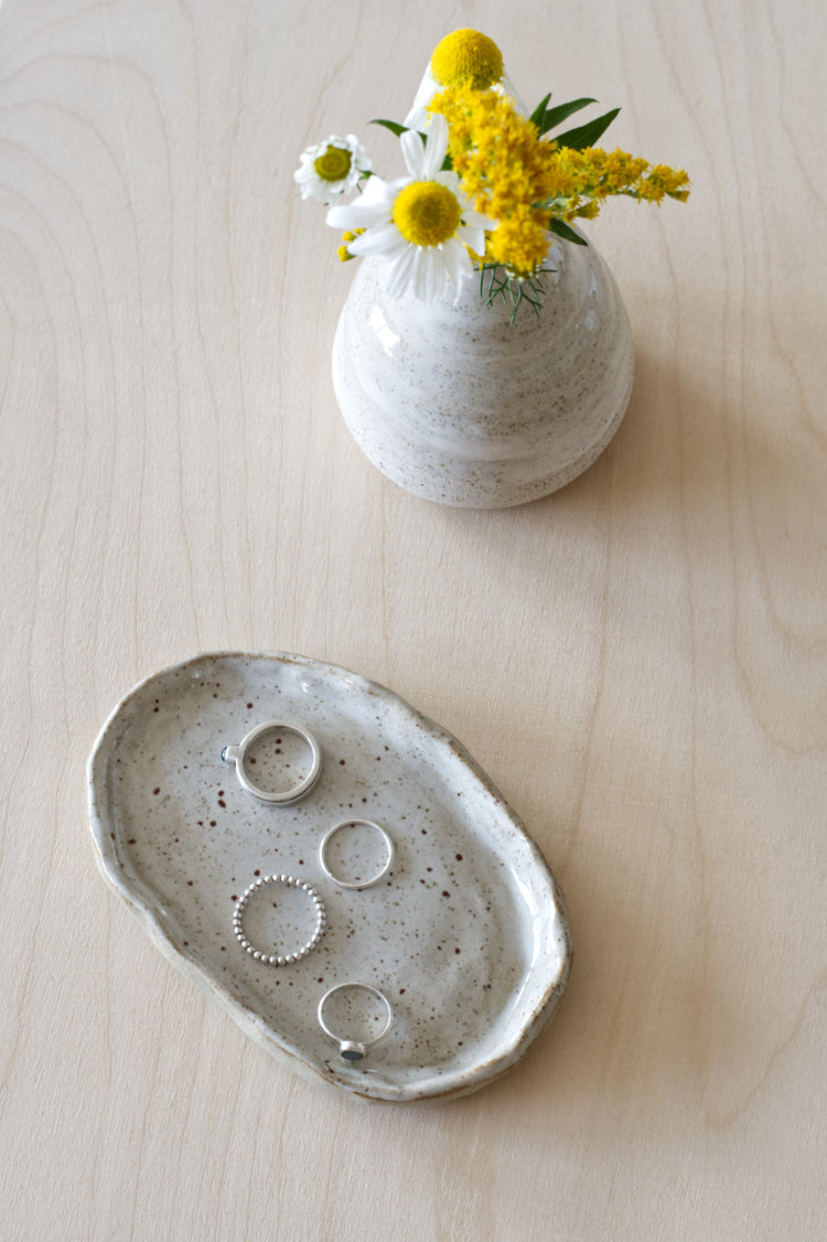 Handgemaakt keramisch schaaltje met ringen naast een klein vaasje met wit-gele bloemen