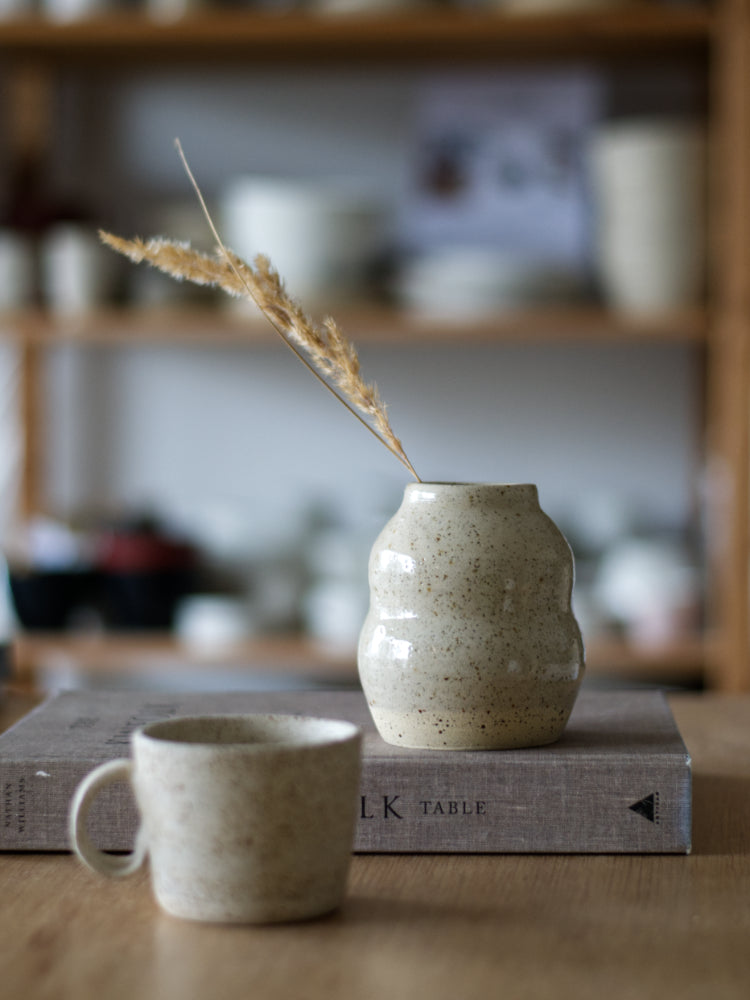 Handgemaakt vaasje gespikkelde klei met glanzend glazuur, op een boek, met een keramiek kopje