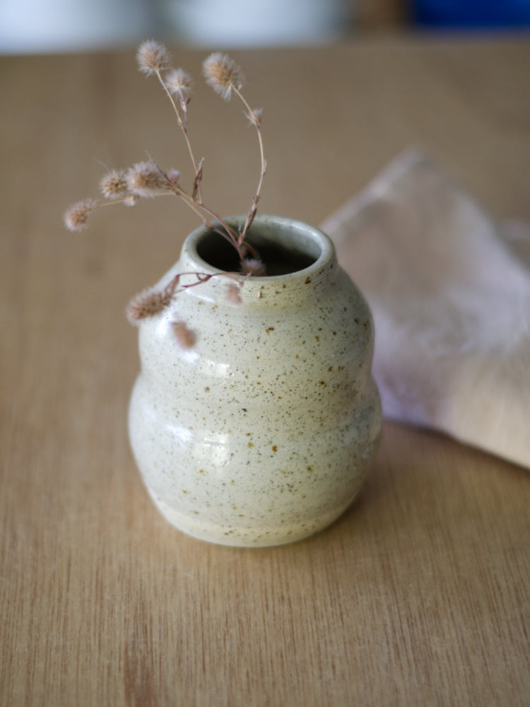 Handgemaakt vaasje gespikkelde klei met glanzend geglazuurde buitenkant met gedroogde bloemen erin op een houten tafel