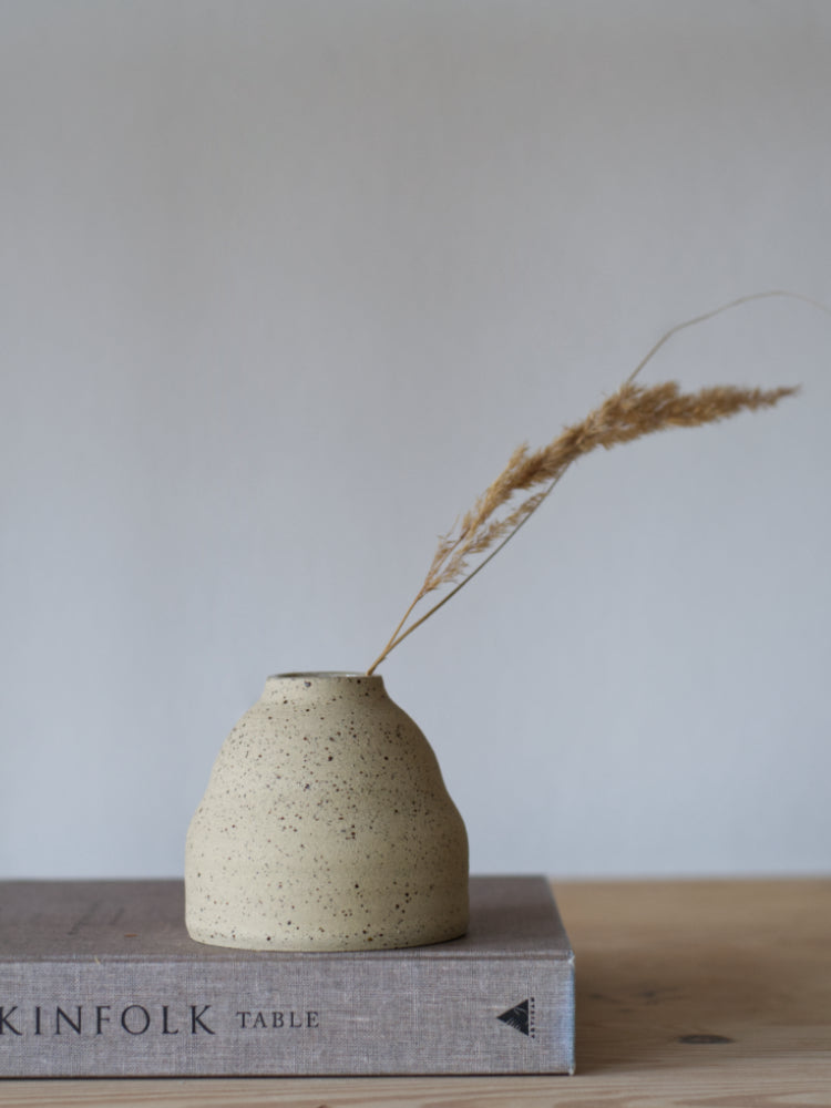 Handgemaakt vaasje van gespikkelde klei ongeglazuurde buitenkant, met graspluim erin, op een kinfolk boek