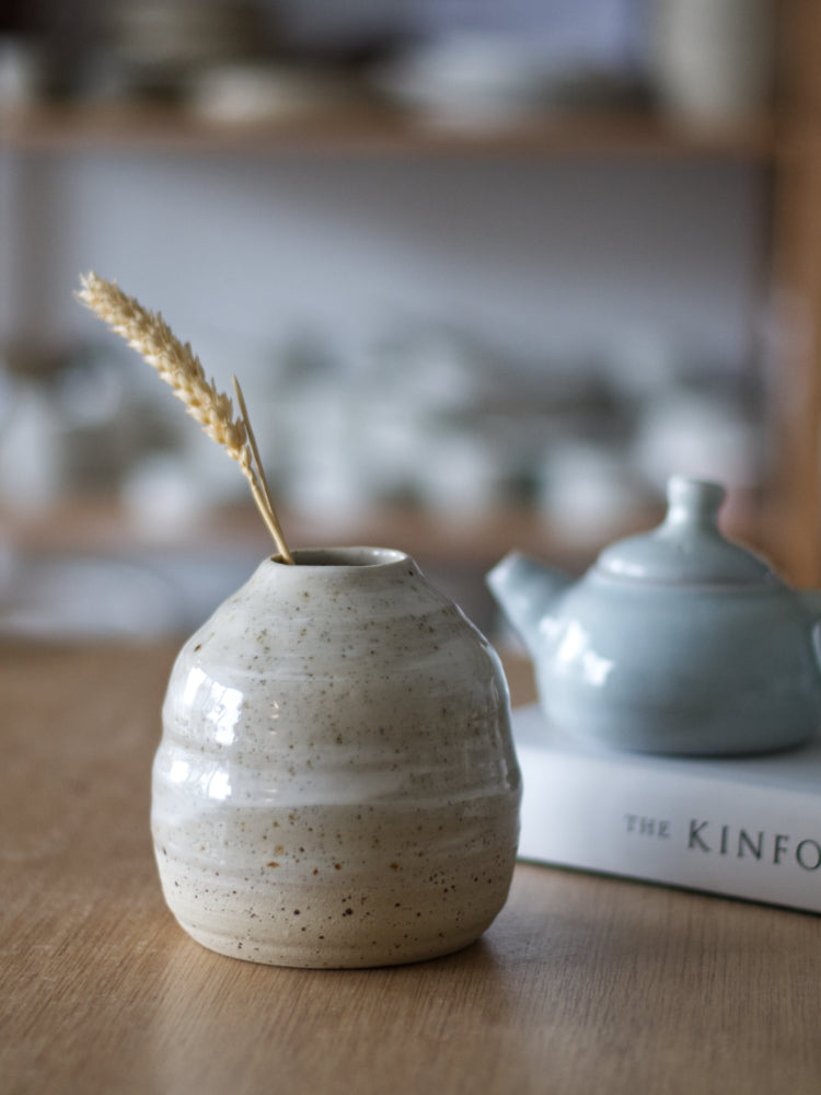 Handgemaakt vaasje van gespikkelde klei met witte slib en glanzend glazuur naast een kinfolk boek met een klein blauw theepotje erop