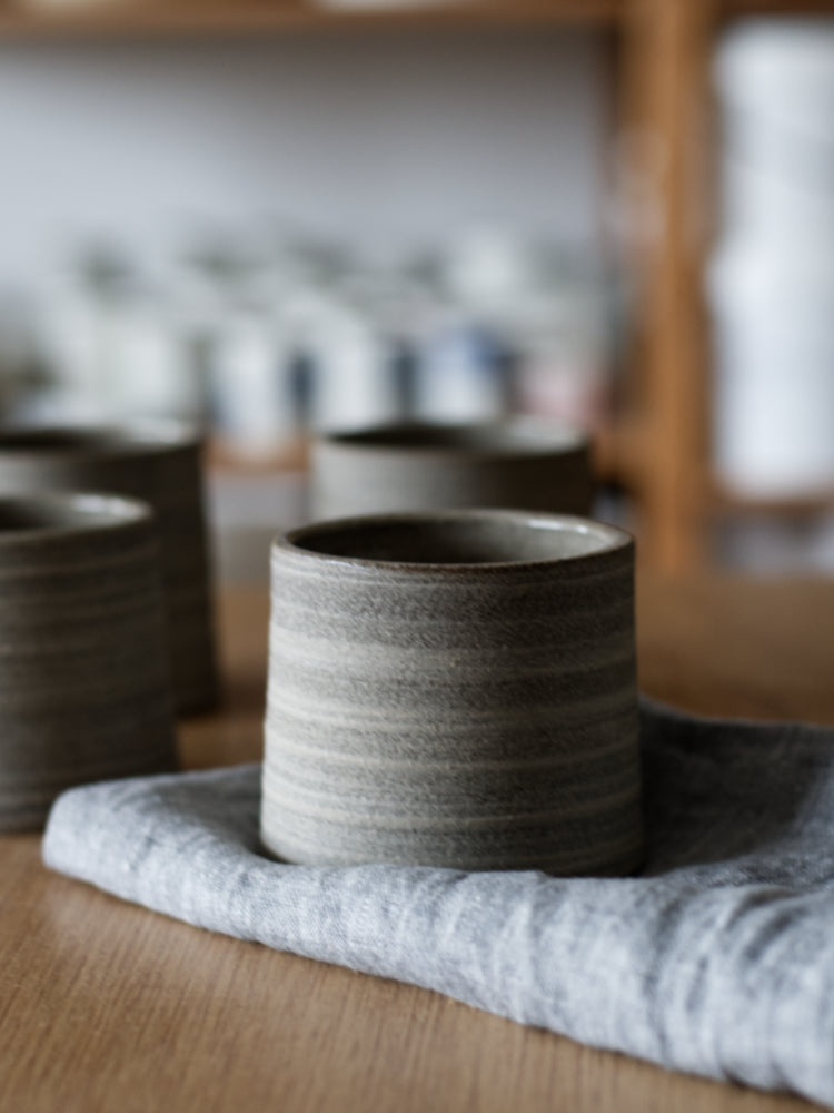 Handgemaakt kopje van bruingrijze klei met ongeglazuurde buitenkant op een blauwe theedoek