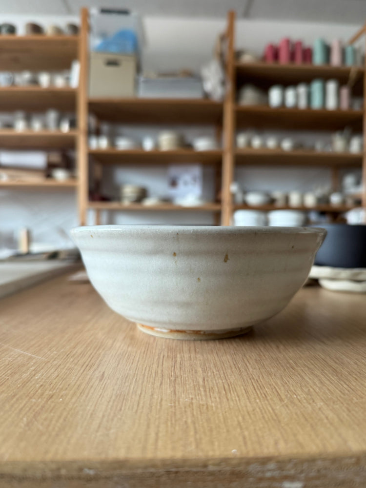 handgemaakte kom met wit glazuur op een houten tafel in het atelier met schappen op de achtergrond