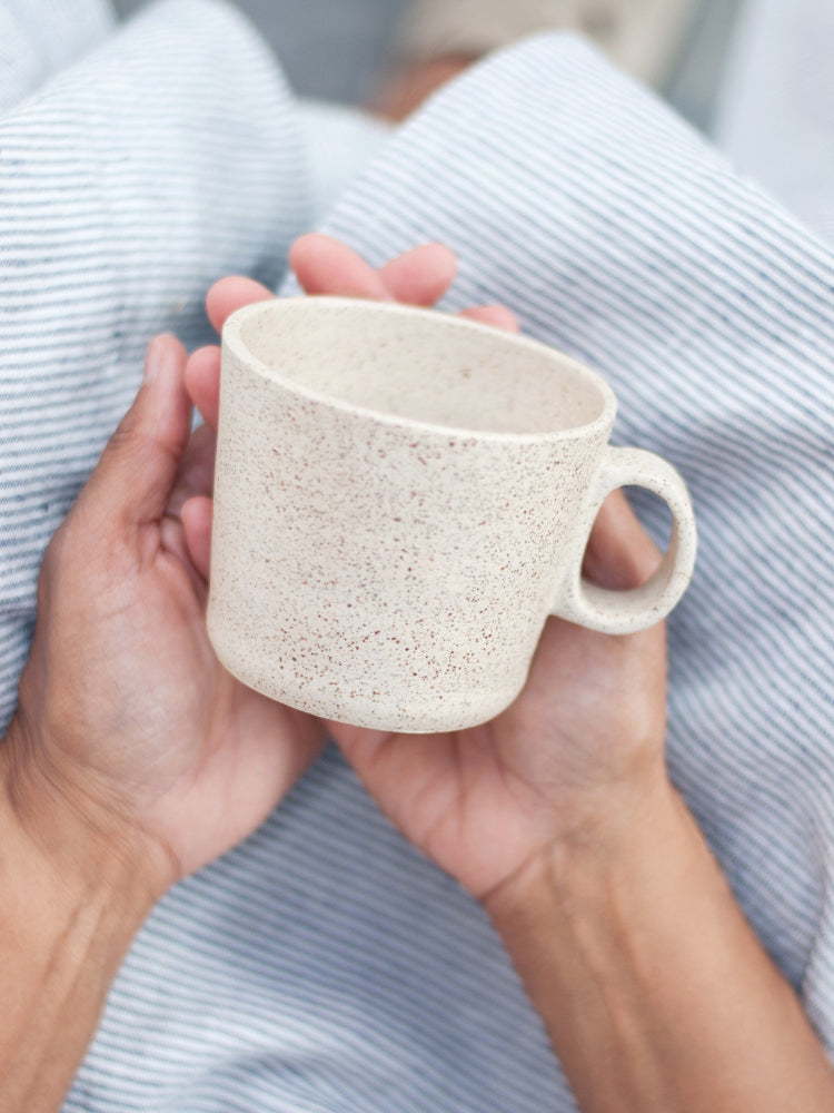 Lichtgespikkeld keramieken mok in de schoot met schort