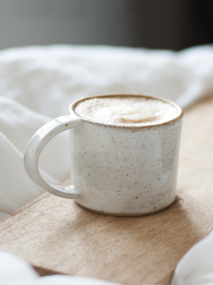 closeup van een handgemaakte whitewashed mok op een houten dienblad op een wit fluffy dekbed
