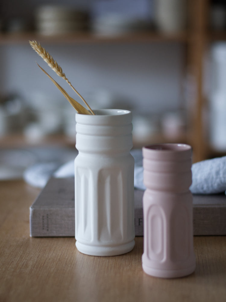 Twee handgemaakte gekleurde porseleinen vaasjes op houten tafel naast een boek en theedoek