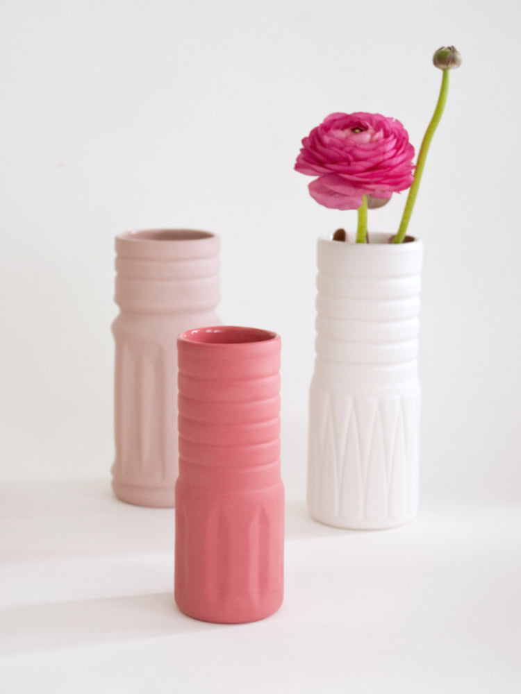 Drie porseleinen vaasjes tegen een witte achtergrond. In een vaasje zit een roze bloem.