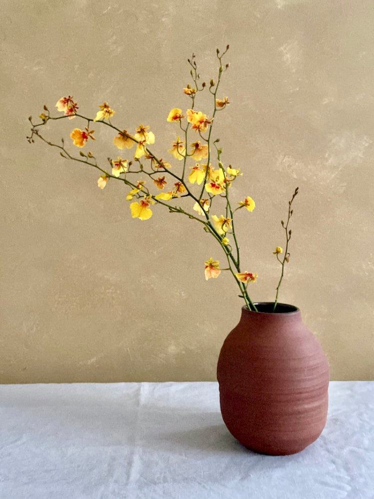 Rode vaas met bloemen, met een lichtbruine achtergrond, heel stijlvol, op een grijsblauw tafelkleed.