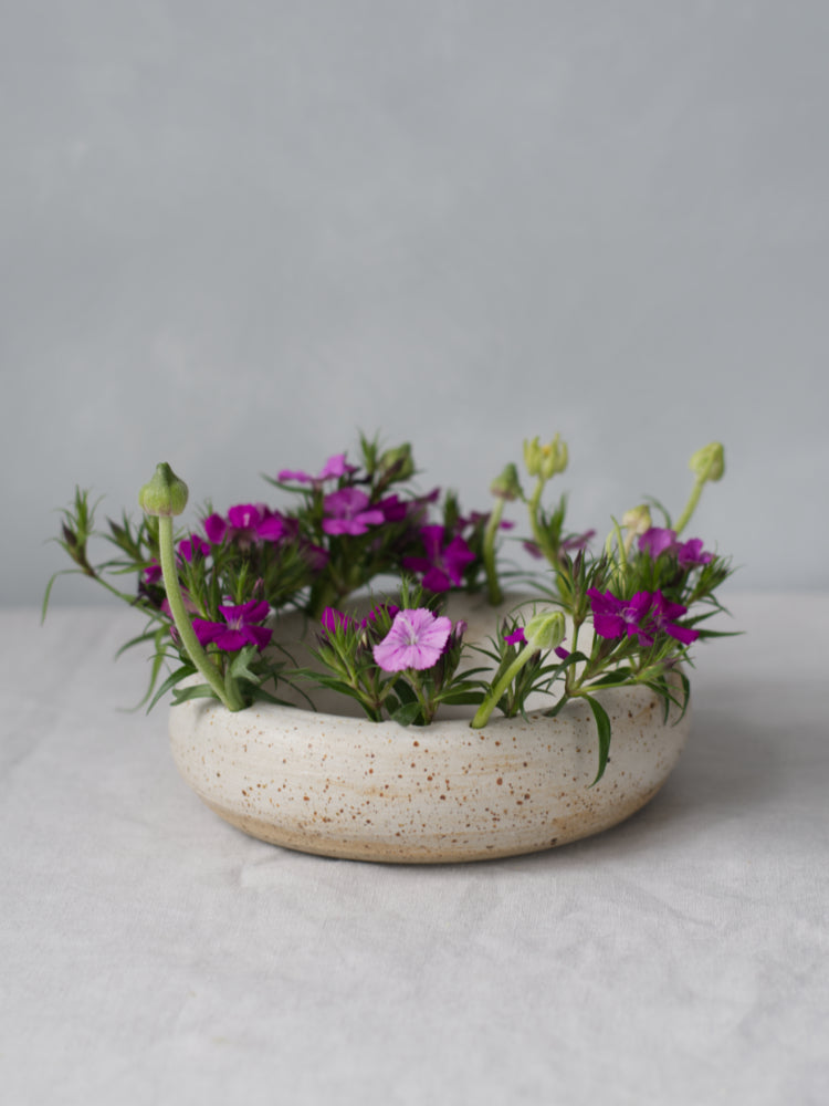 Ronde bloemenvaas whitewashed met roze bloemen op een tafelkleed