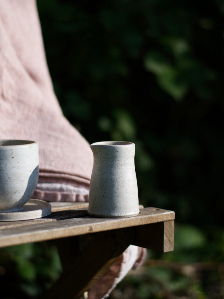 Schenkkannetje op een stoel, buiten, in de zon met een kopje ernaast