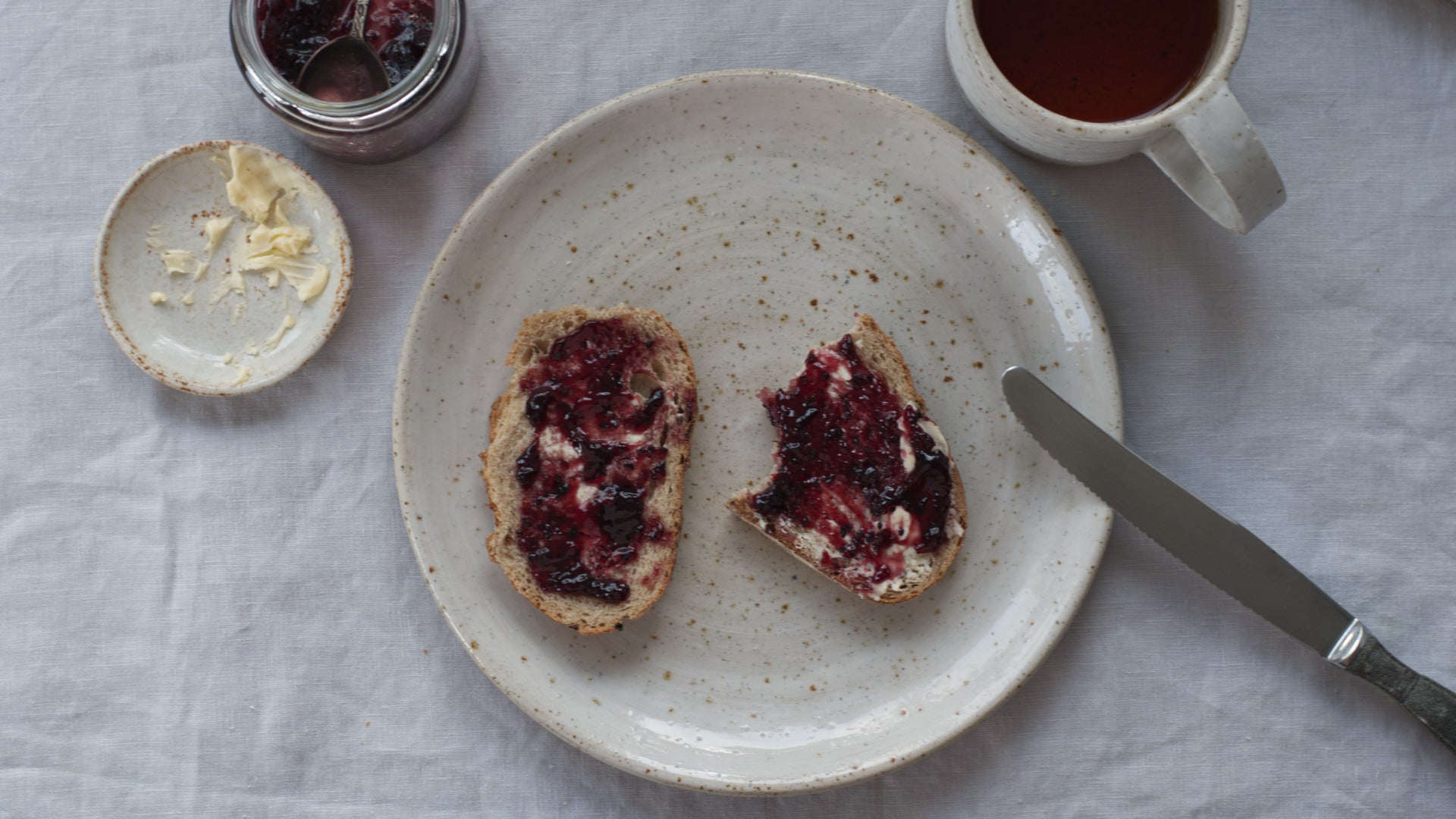 Tafelsetting met handgemaakt bord met boterhammen met jam erop van boven gefotografeerd