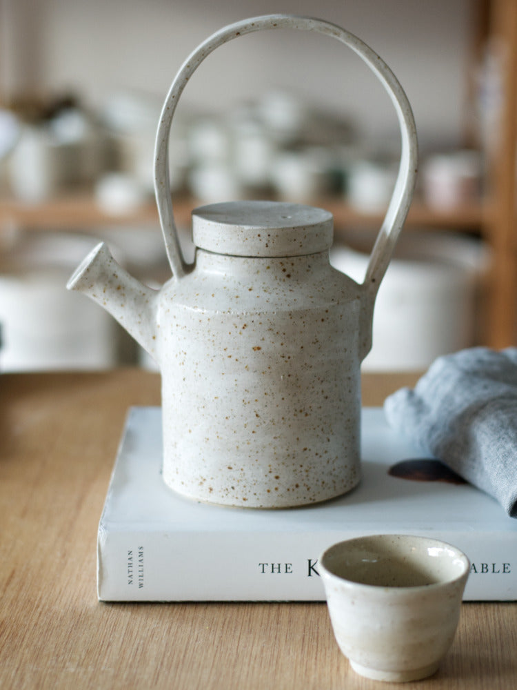 Handgemaakte theepot met whitewashed op boek met theedoek en naast een kopje