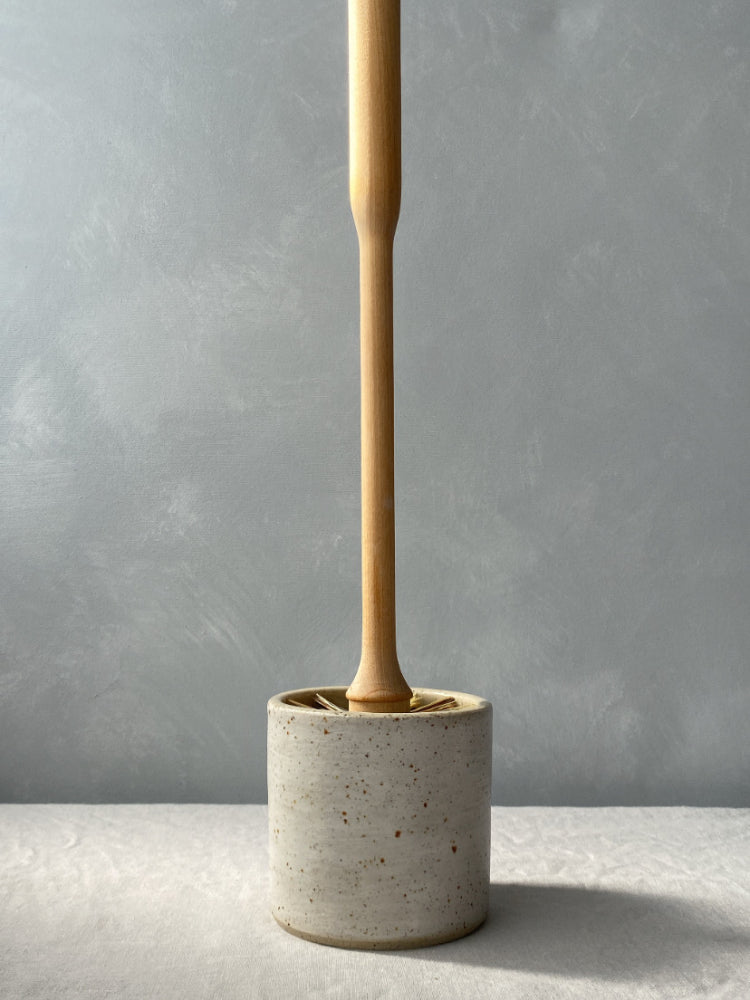 Handgemaakte toiletborstelhouder van gespikkeld keramiek met houten borstel, op een lichtgrijze achtergrond